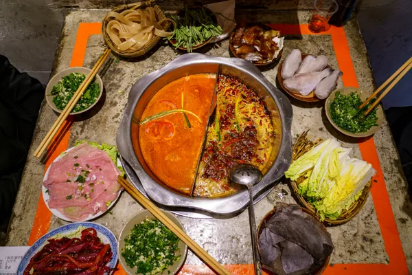 A split Sichuan hotpot with spicy and mild broths surrounded by raw ingredients