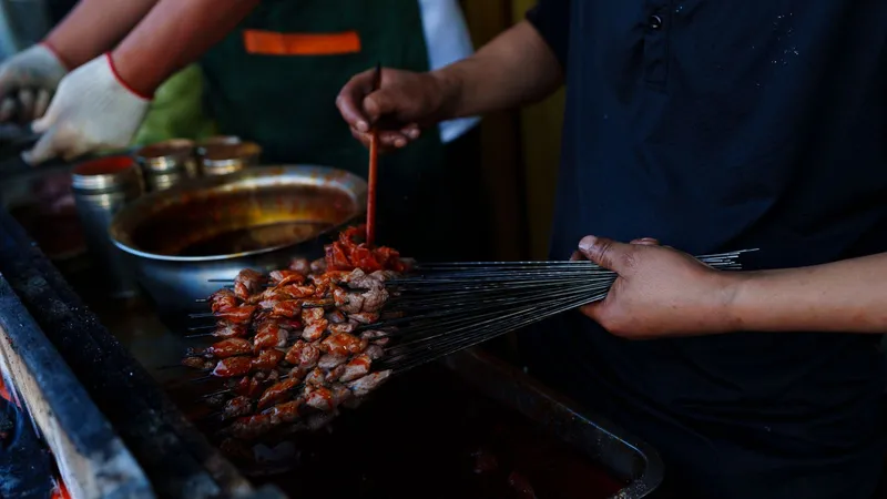 A street vendor saucing bundles of thin lamb skewers over the grill